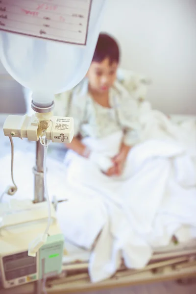 Asian boy sitting on sickbed with infusion pump intravenous IV drip.