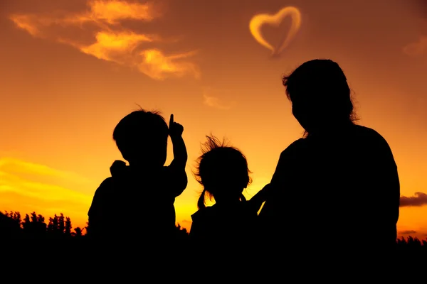 Silhouette of happy family sitting and looking sky at sunset.