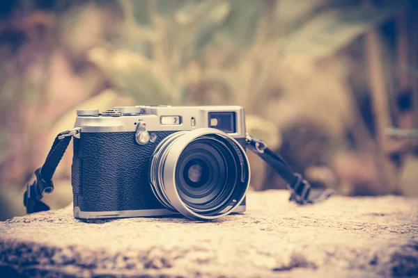 Vintage-style digital camera on boulder over blurred nature back