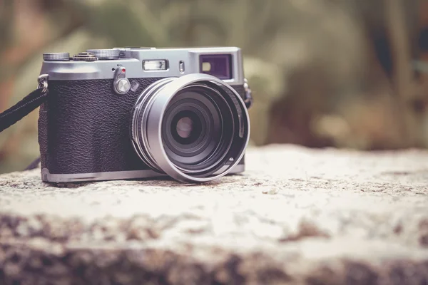 Vintage-style digital camera on boulder over blurred nature back