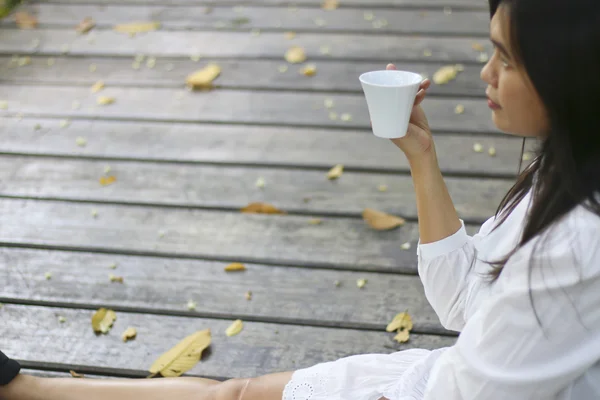 Stock Photo Asian woman drinking coffee in sun sitting outdoor