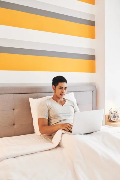 Man sitting in bed with laptop on knees