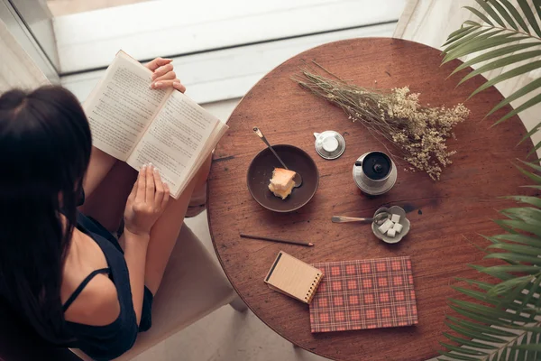 Girl having breakfast and reading textbook