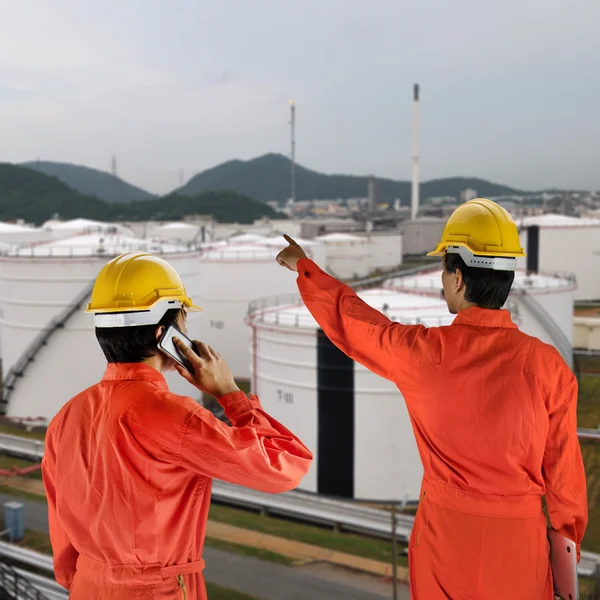 Oil workers in orange uniform and helmet with oil tank