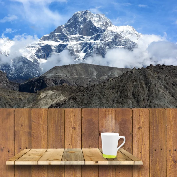 Coffee cup on wood shelve and wood plank with snow mountain back