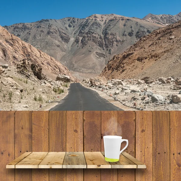 Coffee cup on wood shelve and wood plank with road to mountain i