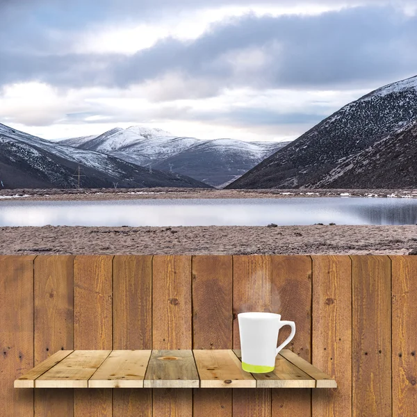 Coffee cup on wood shelve and wood plank with snow mountain back