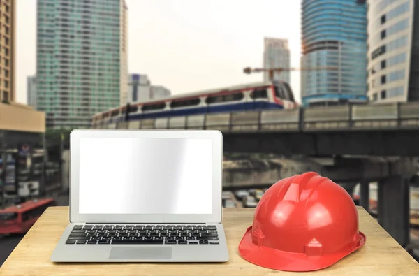 Laptop, hardhat on wood table with modern building