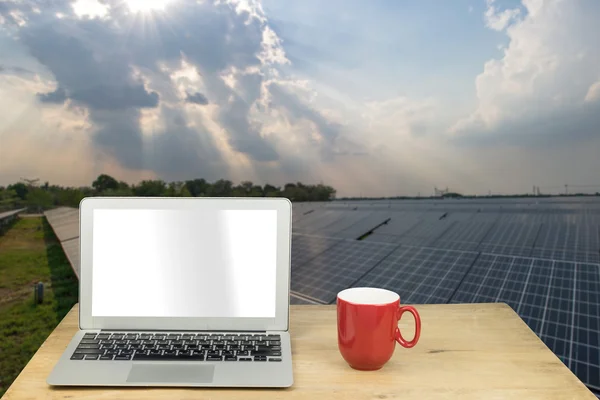 Laptop and red mug on wood table with solar panel