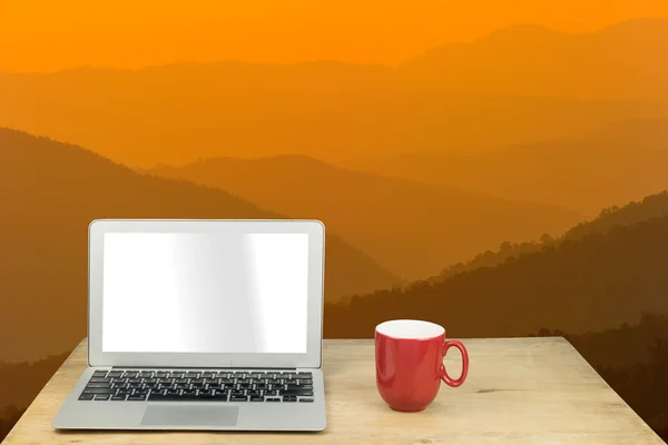 Laptop and red mug on wood table with mountain