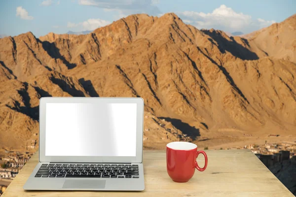 Laptop and red mug on wood table with mountain in Leh Ladakh