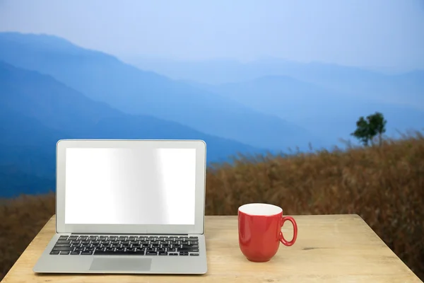 Laptop and red mug on wood table with nature