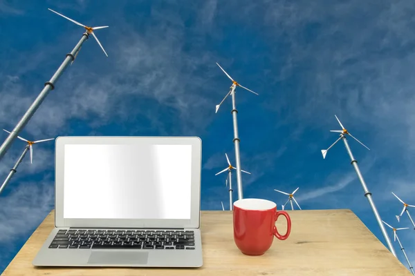 Laptop and red mug on wood table with wind turbine