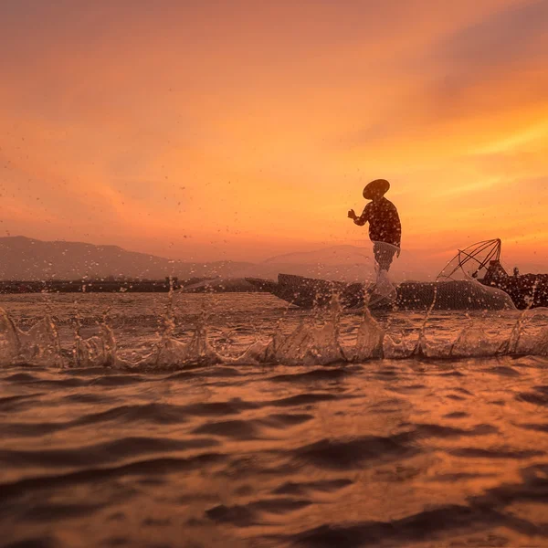 Silhouette of Asian fisherman on wooden boat throwing a net for catching freshwater fish in nature river in the early during sunrise time