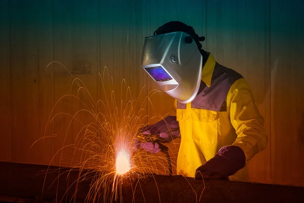 Industrial Worker with safety equipments and protective mask welding steel structure in construction factory.