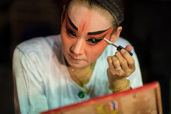 A Chinese opera actress painting mask on her face before the performance at backstage at major shrine in Bangkok\'s chinatown on October 16, 2015 in Bangkok,Thailand