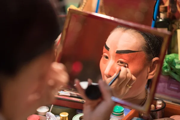 A Chinese opera actress painting mask on her face before the performance at backstage at major shrine in Bangkok's chinatown on October 16, 2015 in Bangkok,Thailand