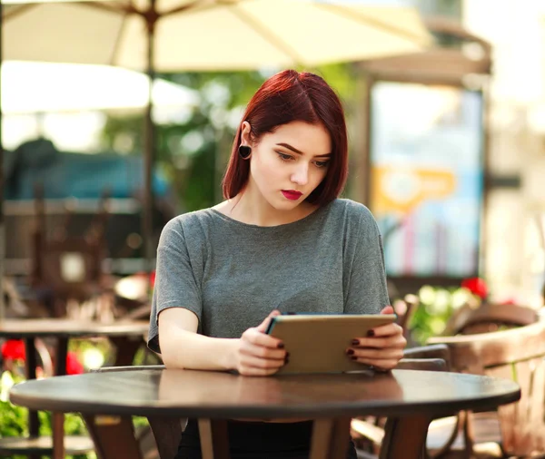 Beautiful girl at table in summer city cafe with tablet