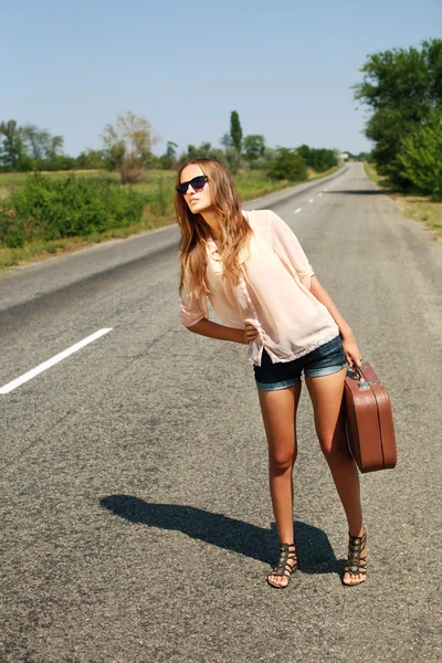 Woman in summer with suitcase hitchhiking on road in countryside