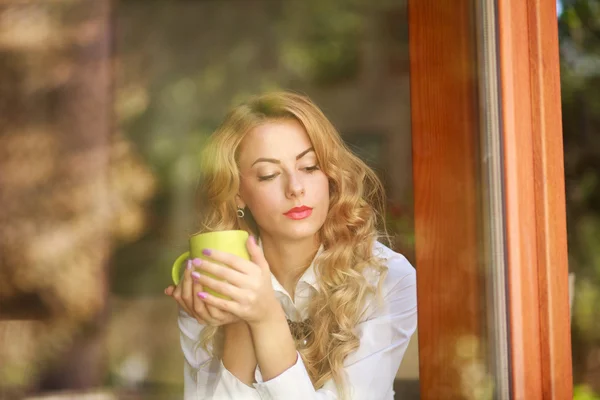 Pensive woman drinking coffee at home, looking out the window