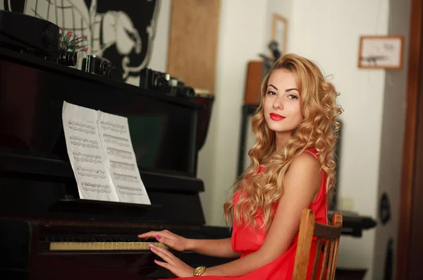 Beautiful young woman sitting at the piano in the room