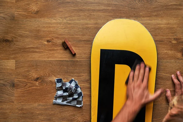 Man rubs snowboard sponge wax on  wooden floor