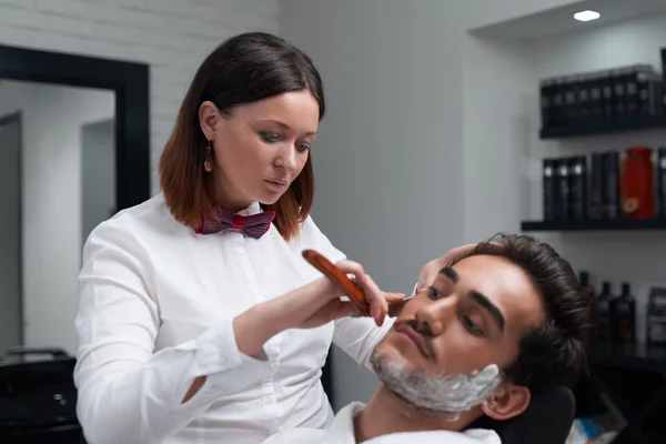 The barber woman carefully shaves beard with razor