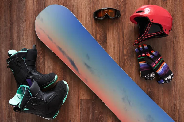 Set of snowboard boots, helmet, gloves and mask on wooden