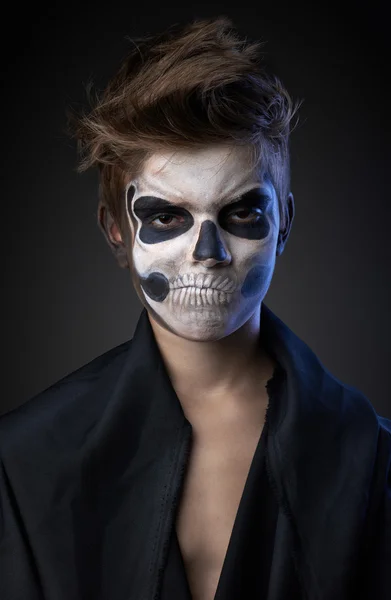 Teen with make-up of the skull in a black cloak unhappy