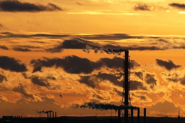 Silhouettes of smoking chimneys. Clouds at sunset in orange evening sky