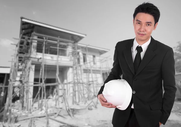 Engineer holding helmet with house construction background
