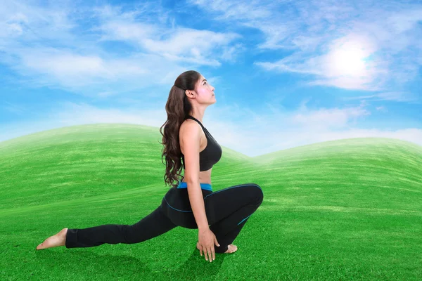 Woman doing yoga exercise on grass with sky