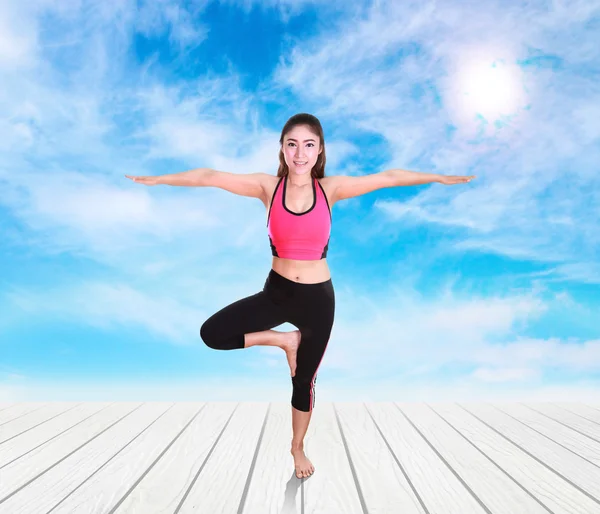 Woman doing yoga exercise on wood floor with sky