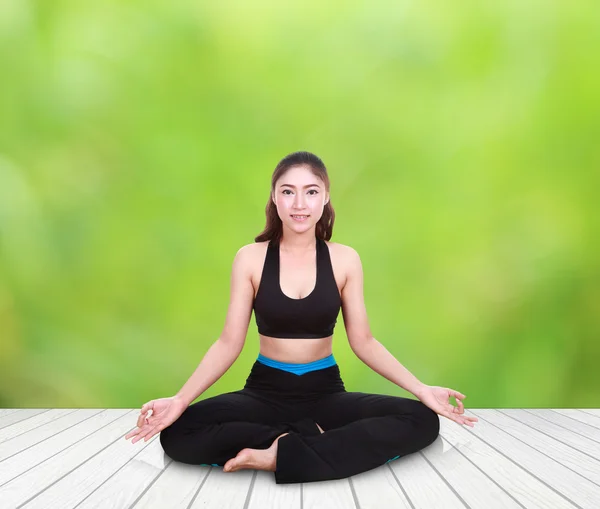 Woman doing yoga exercise on wood floor with natural blur backgr