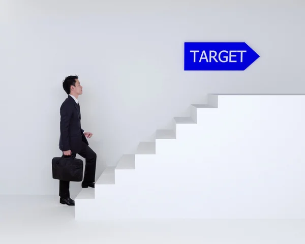 Business man stepping up on stairs to target