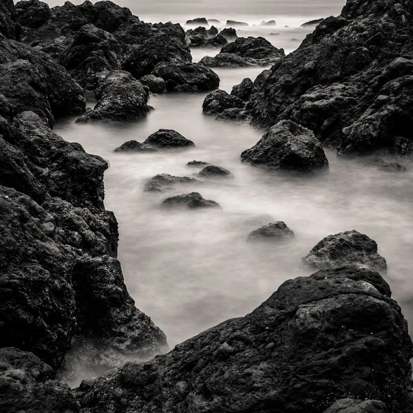 Motion blur water surrounding rocks, black and white