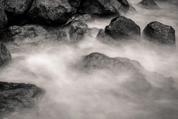 Motion blur water surrounding rocks, black and white