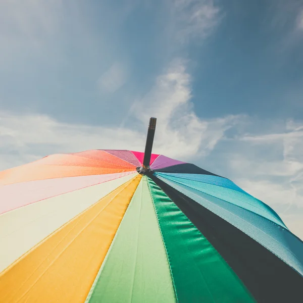 Open colorful rainbow umbrella on blue sky background, vintage look