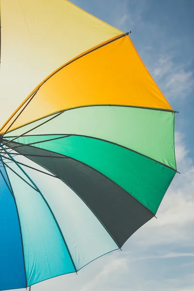 Open colorful rainbow umbrella on blue sky background, vintage look