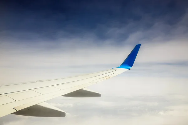 Wing of an airplane flying above the clouds on blue sky background