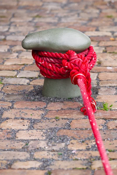 Bollard. Berthing curbstone with the reeled up red rope