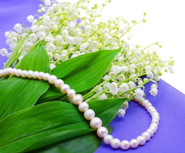 Lilies of the valley an pearl necklace on blue isolated