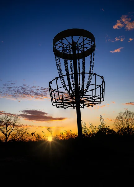 Disc golf basket against sunset