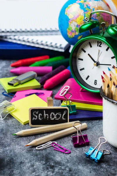 School stationery, pencil, pen, note, alarm clock on grunge chalkboard