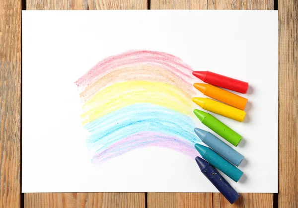 Oil pastel crayons lying on a paper with painted rainbow