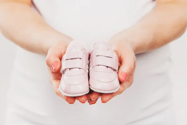 Pregnant woman belly holding pink baby booties, expecting girl. Healthy pregnancy. Maternity and new family concept