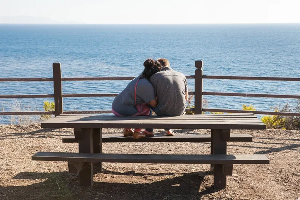 Loving couple sitting on bench watching the ocean, enjoying a beautiful landscape
