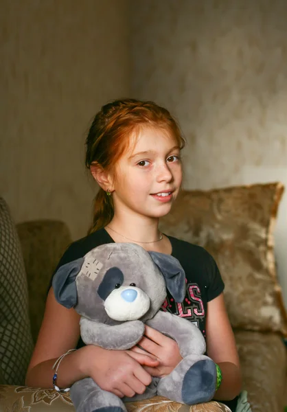 Girl sitting on the sofa hugging a teddy bear.