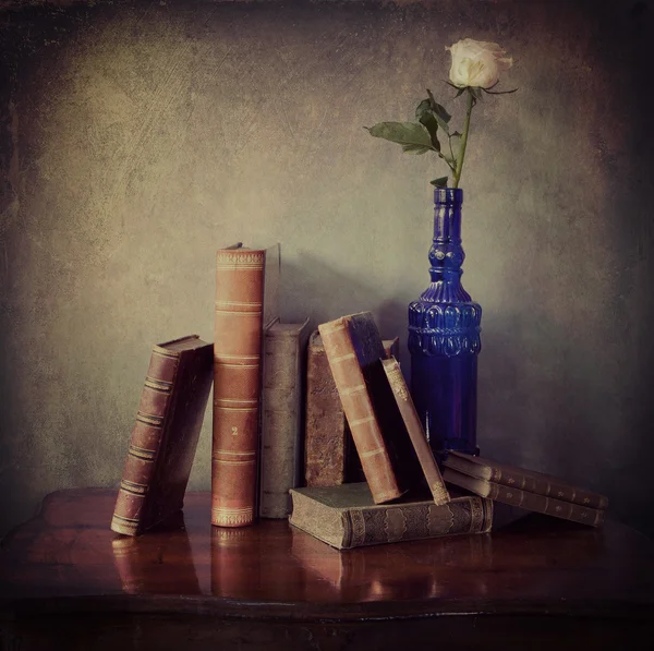Antique books and a pink rose in a blue bottle
