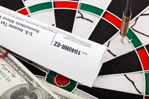 Close up view of red arrow and one hundred dollar bill and US tax form on dart board.